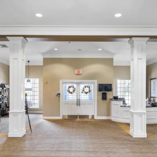 A modern and bright lobby with white pillars, featuring gym equipment and an inviting entrance.