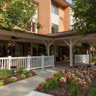 A building exterior with a porch, surrounded by a garden of colorful flowers and trees.