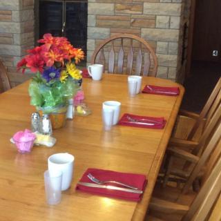 A wooden dining table set with mugs, red napkins, and a colorful bouquet of flowers.