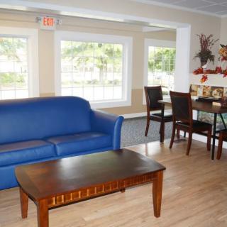 A cozy living room with a blue sofa, wooden coffee table, and dining area by the windows.