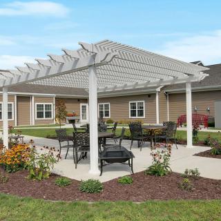 An outdoor patio area with a pergola and seating surrounded by landscaped gardens.