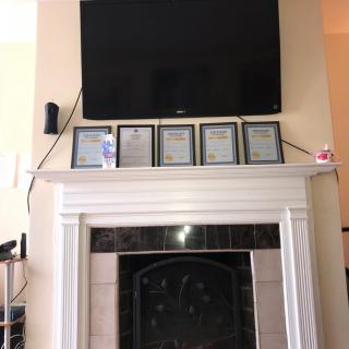 A living room with a large television mounted above a white fireplace mantel, which is decorated with several framed plaques and small items.