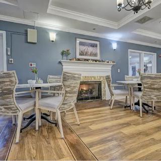 A cozy dining area with a fireplace, featuring wicker chairs and wooden tables on a polished wooden floor.