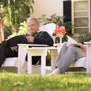 An elderly couple relaxing in the garden while reading on white chairs.