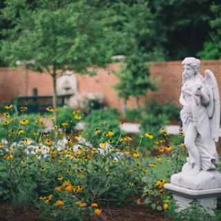 A serene garden adorned with colorful flowers and a majestic angel statue, creating a peaceful atmosphere.