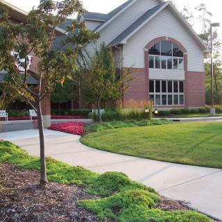A well-maintained lawn and landscaped garden leading to a brick building with large windows.
