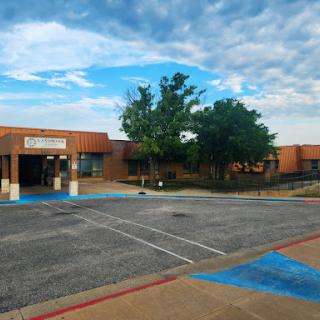 A quiet commercial building set against a cloudy sky, featuring a spacious parking lot with trees nearby.