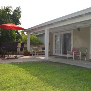 A cozy backyard with a green lawn and a patio featuring outdoor seating under a red umbrella.