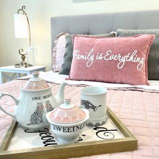 A cozy bedroom setup with a pink pillow and a tea set on a tray.