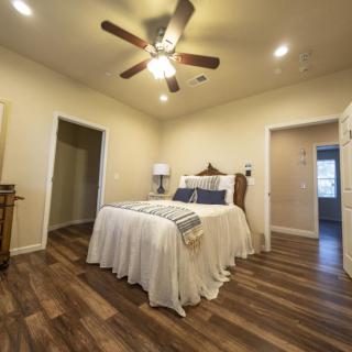A cozy bedroom with a wooden floor, featuring a comfortable bed and ceiling fan.