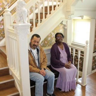 Two people sitting on a bench by a staircase, smiling indoors.