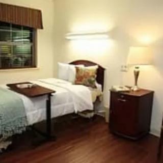 A cozy bedroom featuring a single bed with a wooden headboard, a bedside lamp on a nightstand, and a tray table.