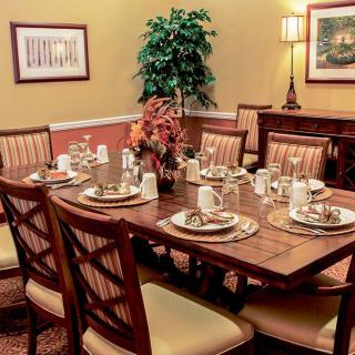 An elegantly set dining table with neatly arranged plates and napkins, surrounded by cushioned chairs in a warmly decorated dining room.
