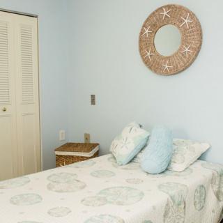 A cozy bedroom with a neatly made bed, light blue walls, and a decorative mirror above the headboard.