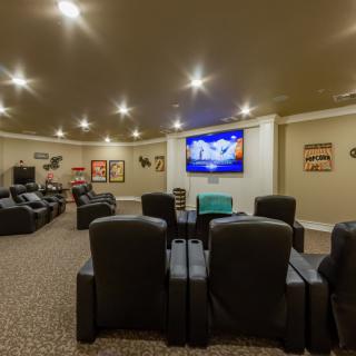 A spacious home theater room with comfortable recliners, a large screen TV, and decorative wall art.