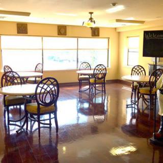 A brightly lit dining area with several tables and chairs, featuring large windows and polished floors.