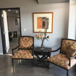 A cozy waiting area featuring two upholstered chairs, a small table with a vase of flowers, and a framed artwork on the wall.