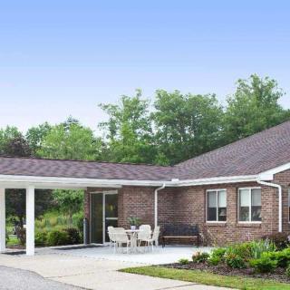 A brick residential building with a covered driveway and outdoor seating area, surrounded by greenery.