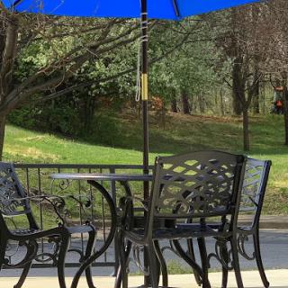 A cozy outdoor seating area with a table and chairs shaded by a blue umbrella, surrounded by lush greenery.