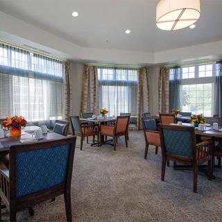 A well-lit dining room with multiple tables and chairs, featuring large windows and elegant decor.