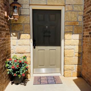 A welcoming entrance featuring a door surrounded by stone walls, with a potted plant and doormat in front.