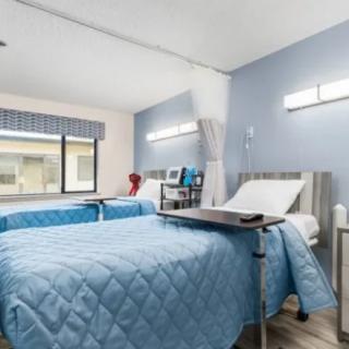 A clean and organized hospital room with two beds, featuring blue bedding and medical equipment.