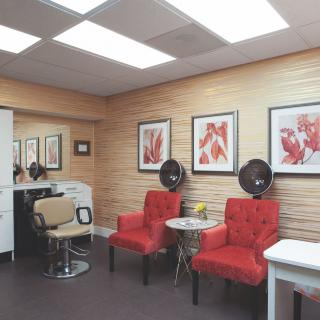 A cozy salon interior featuring red chairs, hair dryers, artwork on the walls, and mirrors under bright lighting.