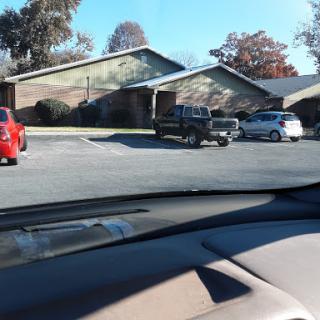 A view of a parking area in front of residential buildings, showcasing various vehicles parked.