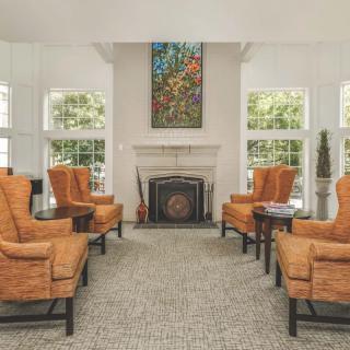 A cozy living room with orange armchairs arranged around a fireplace, complemented by a decorative painting above.