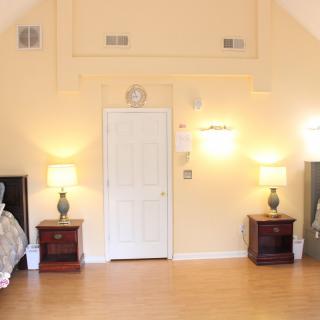 A spacious bedroom with two nightstands and lamps, featuring a central door and wooden flooring.