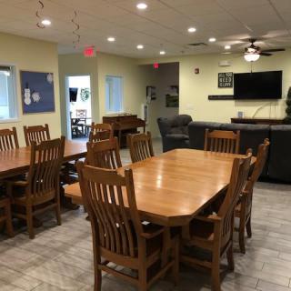A spacious meeting room with a large wooden table, multiple chairs, a wall-mounted TV, and a ceiling fan.
