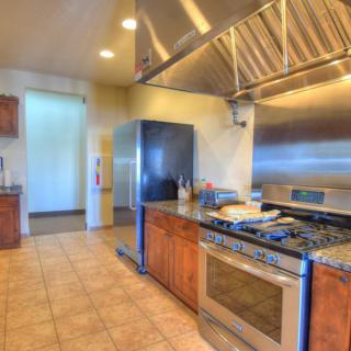 A modern kitchen featuring stainless steel appliances and a large gas stove with wooden cabinets and tile flooring.