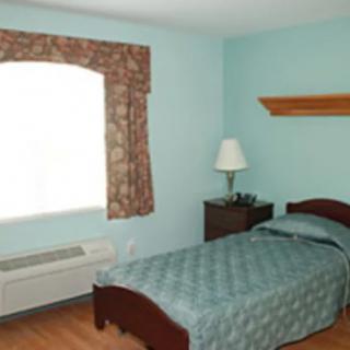 A simple bedroom with a single bed, nightstand, lamp, and an air conditioner by the window.