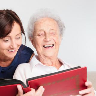 An elderly person and a caregiver enjoying a book together, sharing smiles and warmth.