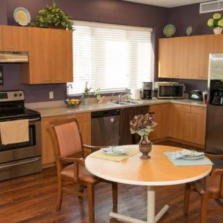 A modern kitchen with wooden cabinets, stainless steel appliances, and a small dining area with a round table and chairs.
