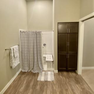 A spacious bathroom featuring a shower with a curtain, wooden cabinet, and neatly arranged towels on the rack.