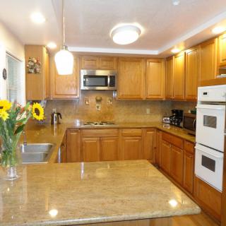 A modern kitchen with wooden cabinets and a marble countertop, featuring appliances like an oven and microwave.