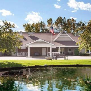 A scenic view of a building with a pond and trees in the foreground, set against a clear blue sky.