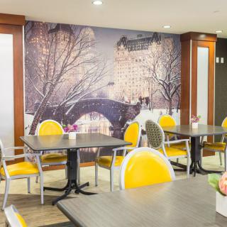 A cozy cafe interior featuring yellow chairs and a large mural of a winter cityscape.