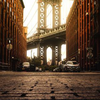 A stunning view of the Brooklyn Bridge framed by charming cobblestone streets, capturing the essence of urban life during golden hour.