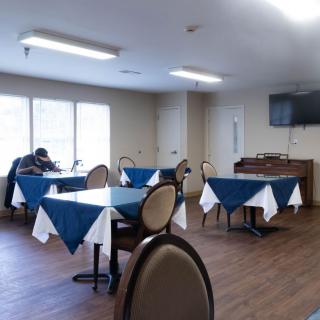An empty dining room with tables and chairs, featuring blue tablecloths and a television on the wall.