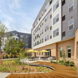 A modern apartment complex with an outdoor patio area featuring yellow umbrellas and well-maintained landscaping.