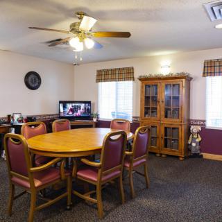 A dining room features a round table with chairs, a wooden cabinet, and a television.