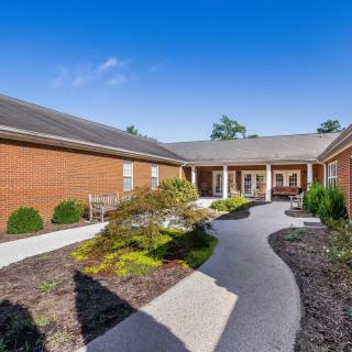 A well-maintained brick building with a curved pathway and landscaped greenery under a clear blue sky.