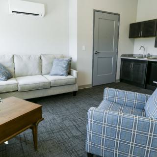 A modern living room with a sofa, armchair, and kitchenette.