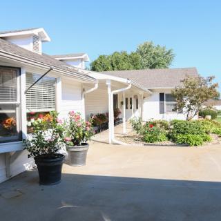 A bright, sunny day emphasizes the charming exterior of a house with a welcoming patio and lush garden.
