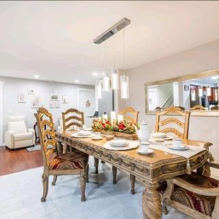 An elegant dining room featuring a wooden table with intricate carvings, surrounded by matching chairs. The table is set for a meal, and decorative lighting hangs above, enhancing the sophisticated ambiance.