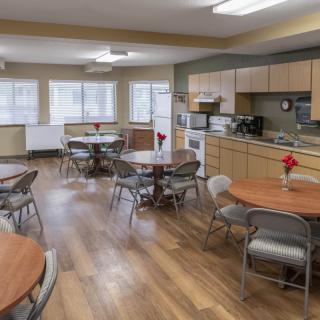 A modern kitchen and dining area with round tables and metal chairs, featuring wooden flooring and bright natural light.