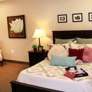 A cozy bedroom with decorative pillows, a bedside lamp, and artwork on the walls.
