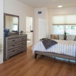 A modern bedroom with a wooden floor, featuring a bed and dresser.